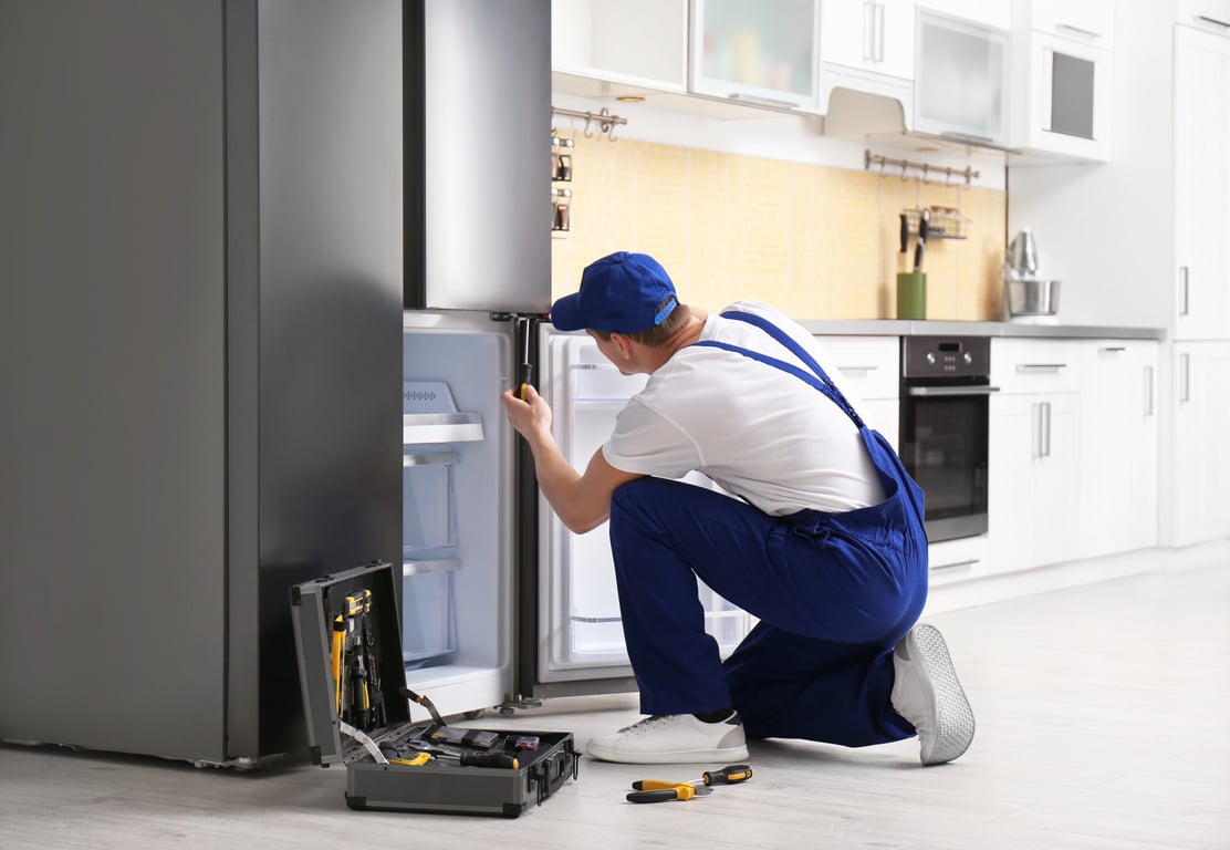 Male Technician with Screwdriver Repairing Refrigerator in Kitchen